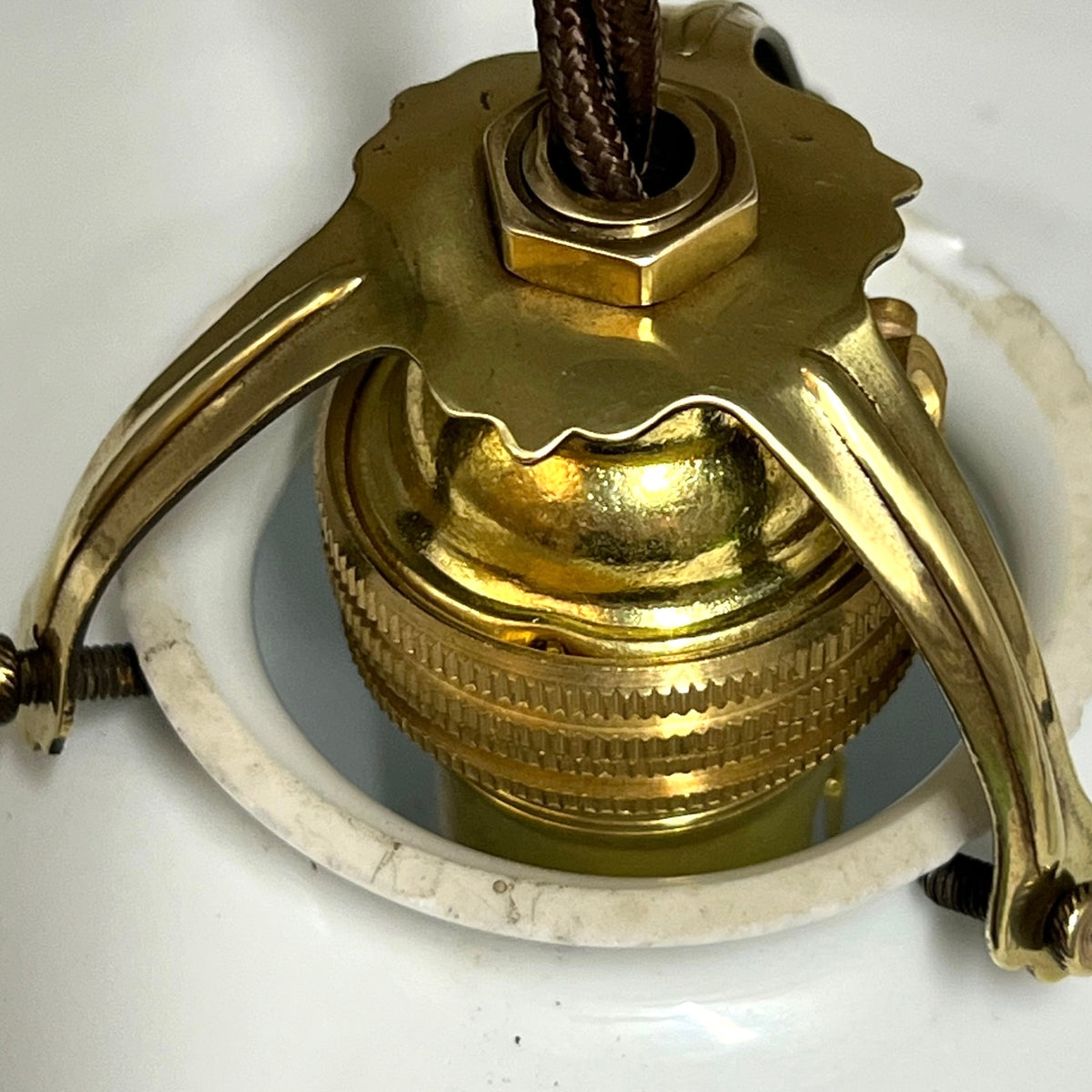 A close-up of a vintage brass ceiling light fixture component, featuring a polished brass canopy, decorative metal arms, and a white ceramic downrod.