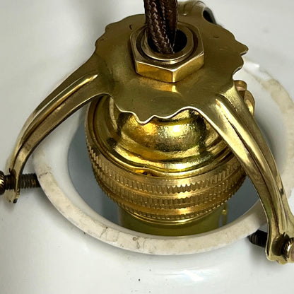 A close-up of a vintage brass ceiling light fixture component, featuring a polished brass canopy, decorative metal arms, and a white ceramic downrod.