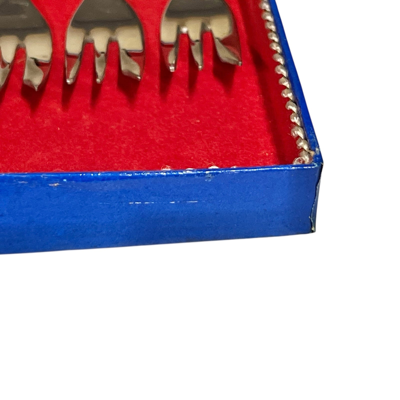 Close-up of a red and blue box containing 12 French dessert forks on a white background