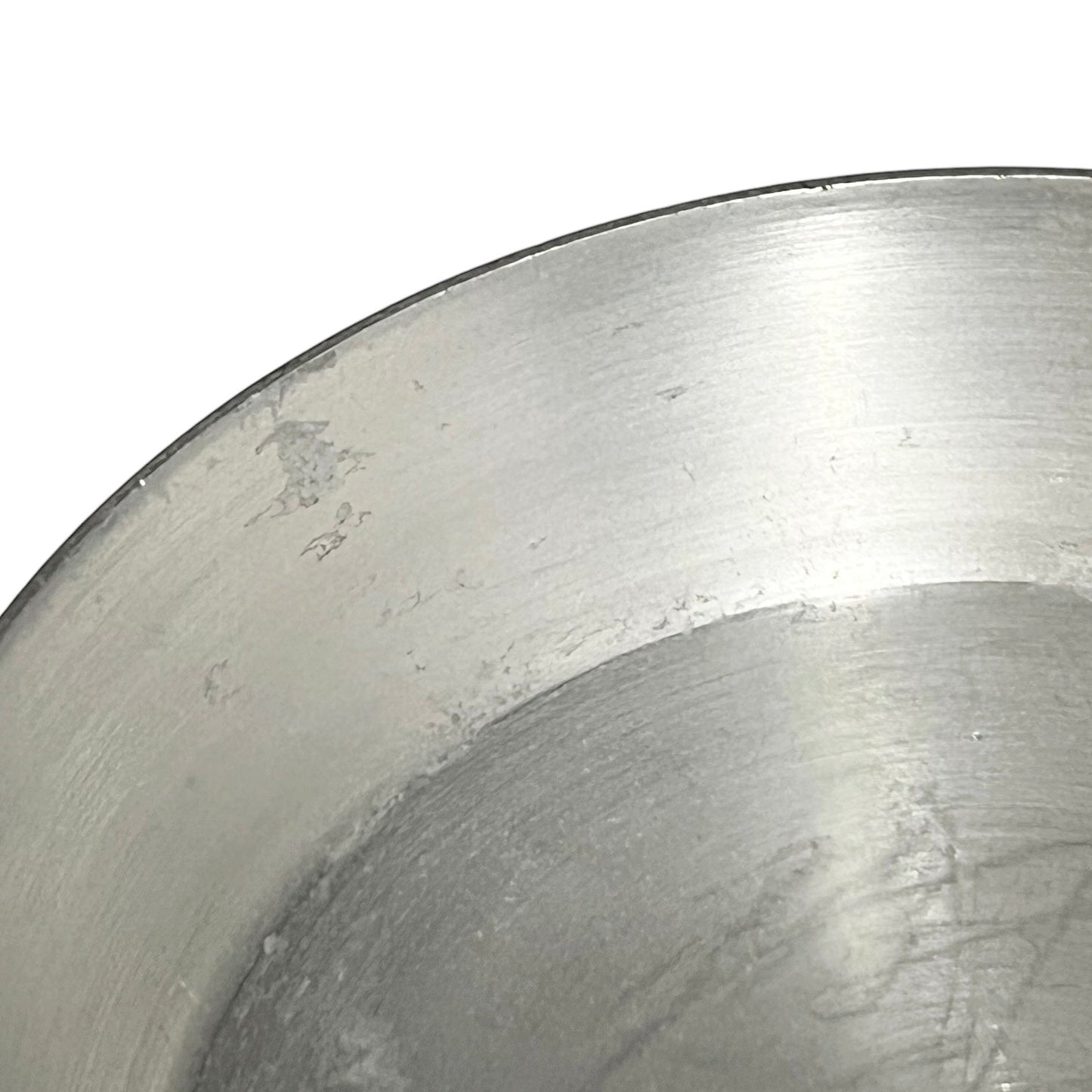 Close-up of the interior of a brushed metal bowl or pan with a silver metallic finish and visible surface scratches, against a white background.