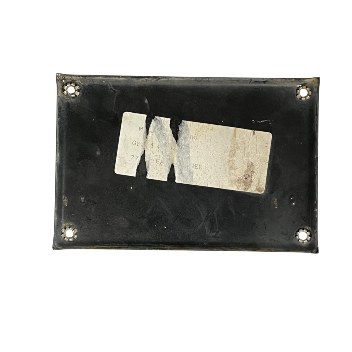A black rectangular metal plate with rounded corners, four screw holes, and a worn white paper label in the center, photographed on a plain white background.