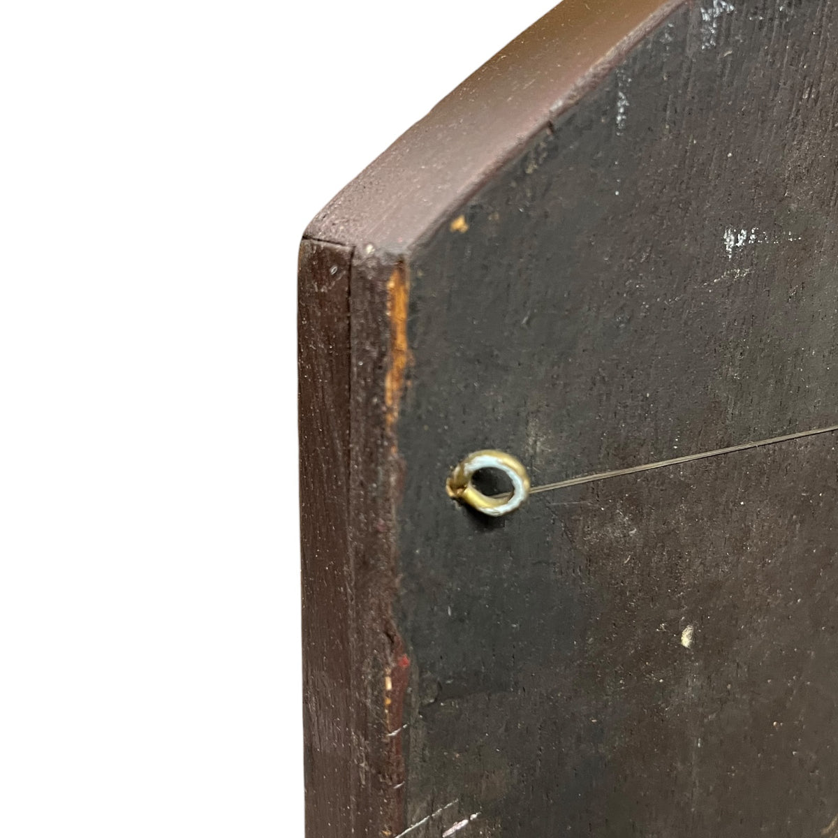 Close-up of a dark brown wooden panel or board corner with a small metal loop and a thin horizontal wire extending from it, photographed against a white background.