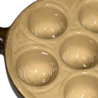 Close-up of a brown snail plates with deep oval wells, showing a glossy glazed finish and a dark brown handle on a white background.