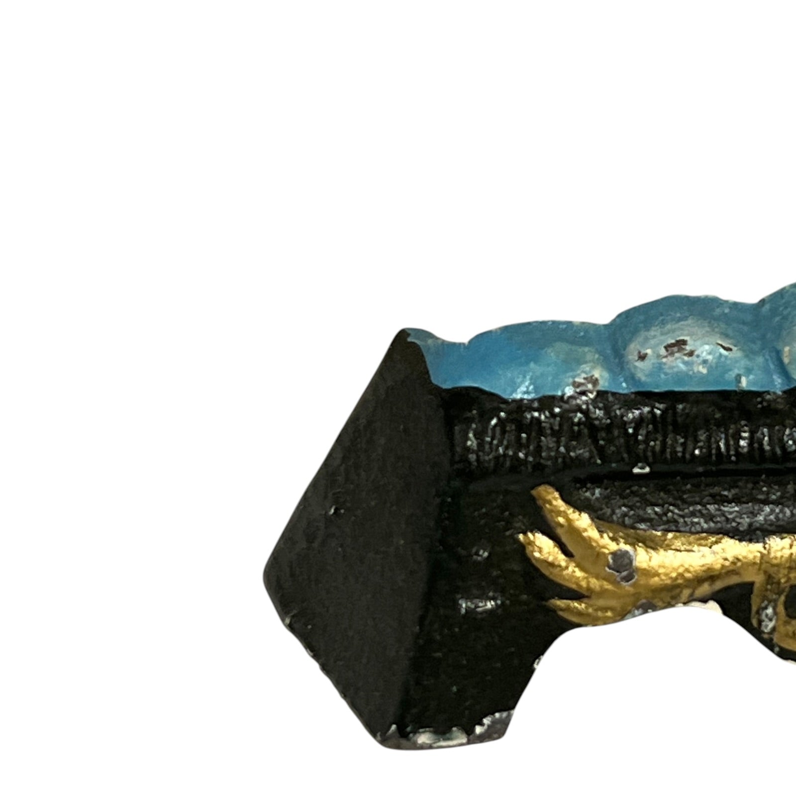 A close-up of a decorative object with a black textured base, a blue top section, and a gold hand detail, shown against a plain white background.