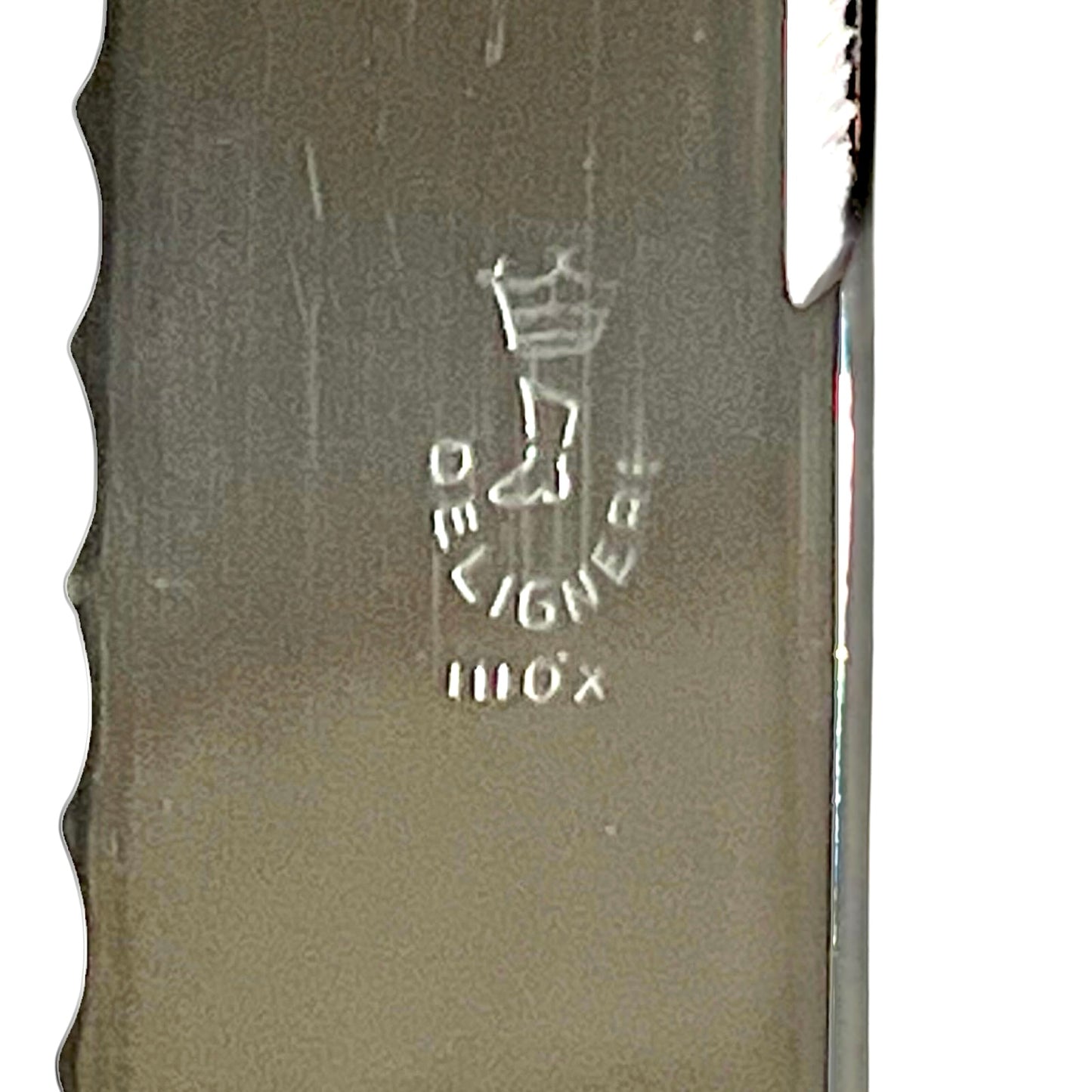 Close-up of a metallic knife blade showing the engraved Deligne logo and a serrated edge on a white background.