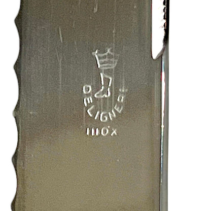 Close-up of a metallic knife blade showing the engraved Deligne logo and a serrated edge on a white background.