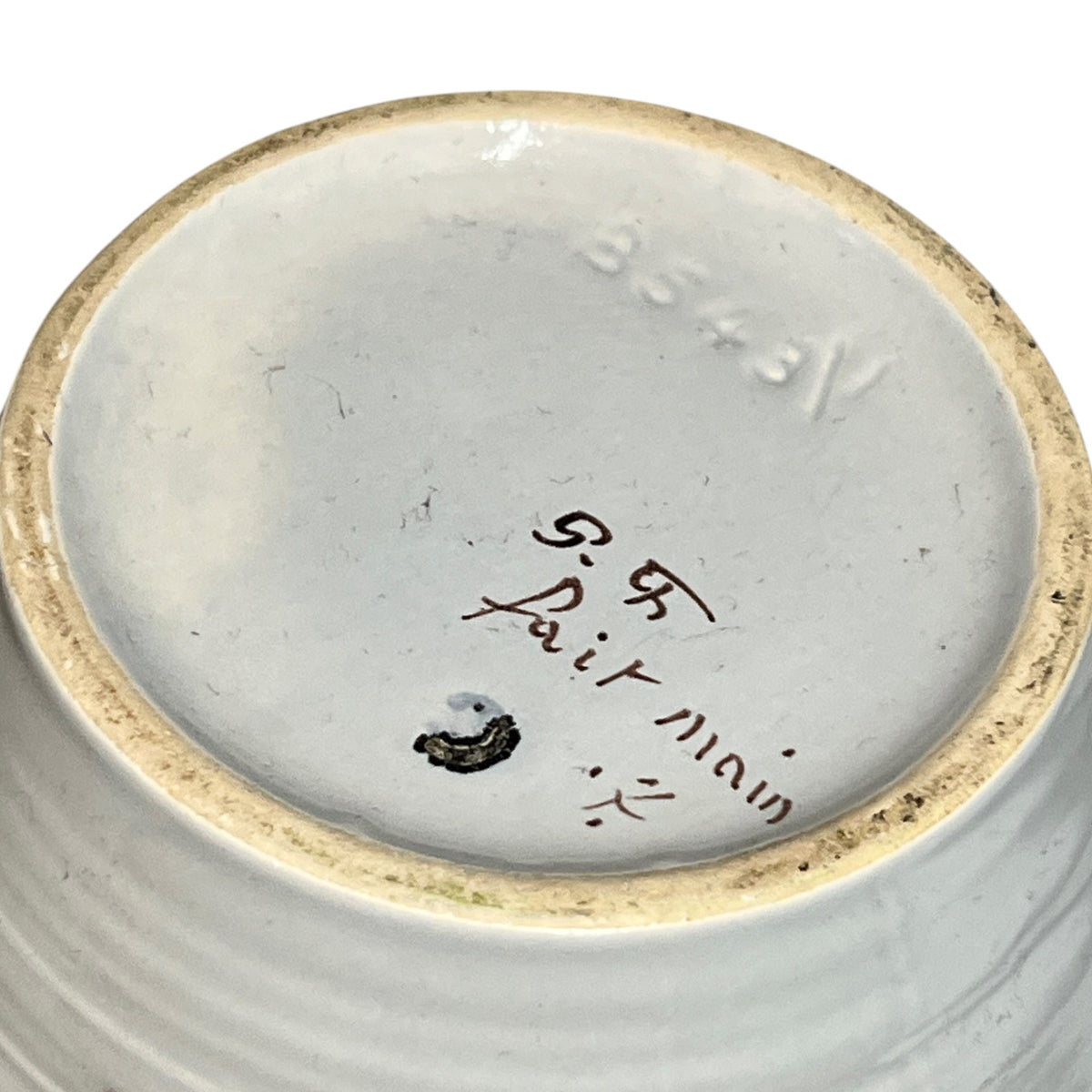 Close-up of the bottom of a ceramic bowl or vase, showing a light gray glazed interior with a natural beige rim, hand-written maker's marks reading 'P. R.