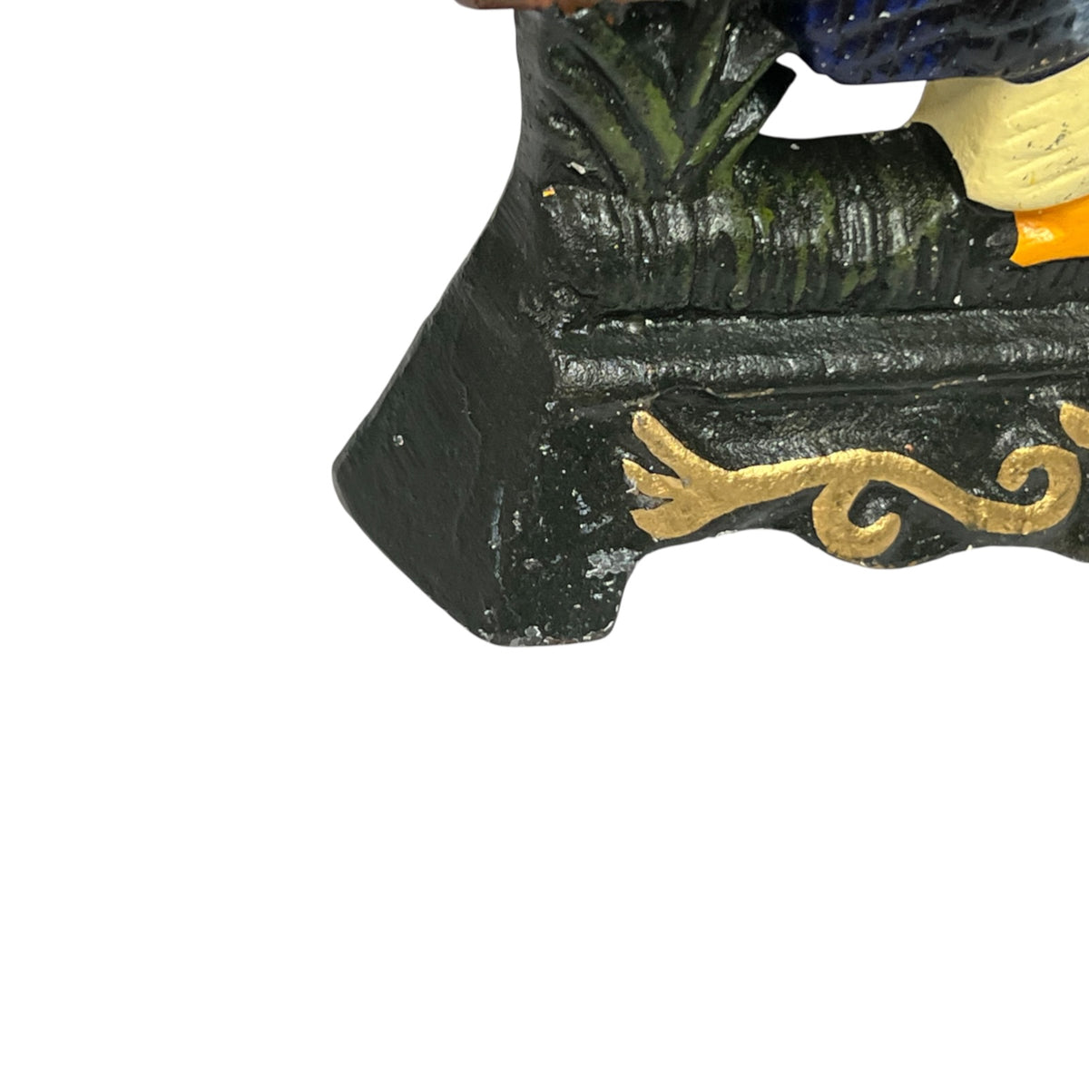 Close-up of a decorative figurine or statue base in black with gold scrollwork and a small portion of blue and cream visible above, isolated on a white background.
