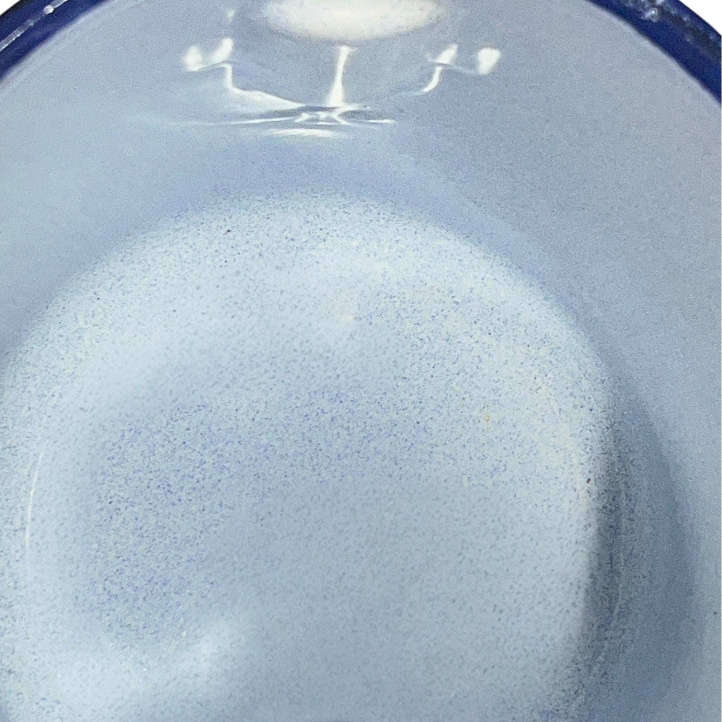 Close-up of a light blue speckled enamel surface with a glossy finish and a dark blue rim visible at the top edge.