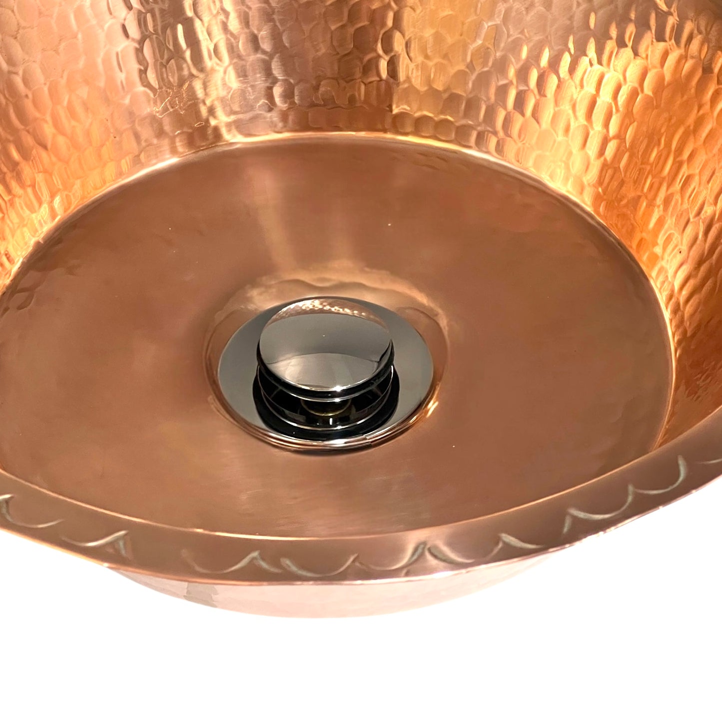Close-up of a copper sink basin with decorative patterns on a white background