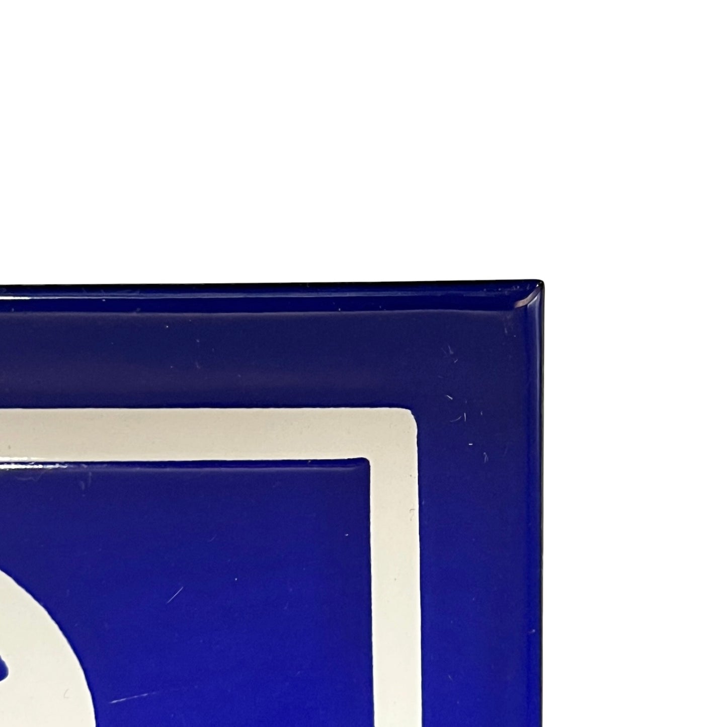 Close-up of a glossy deep blue sign with a white border and partial white graphic detail, photographed against a white background.