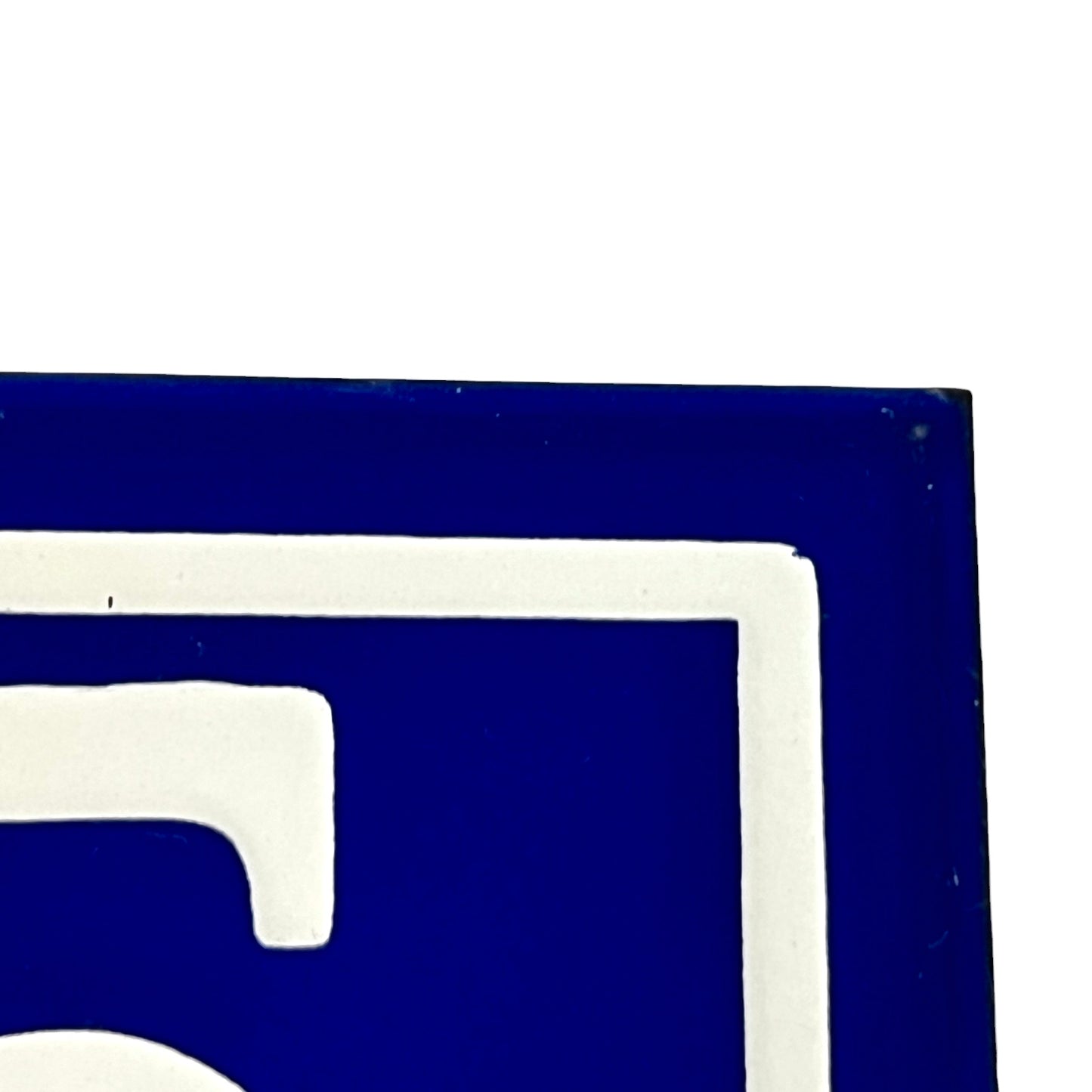 A close-up corner of a blue and white sign or panel, showing a dark blue field with a white border and partial white symbol on a white background.
