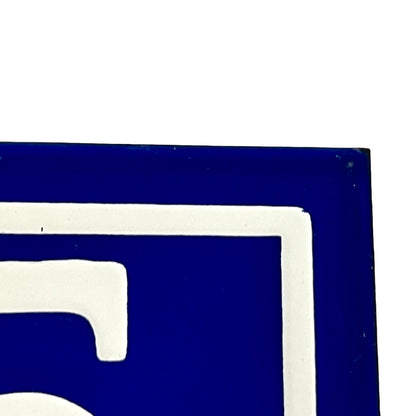 A close-up corner of a blue and white sign or panel, showing a dark blue field with a white border and partial white symbol on a white background.