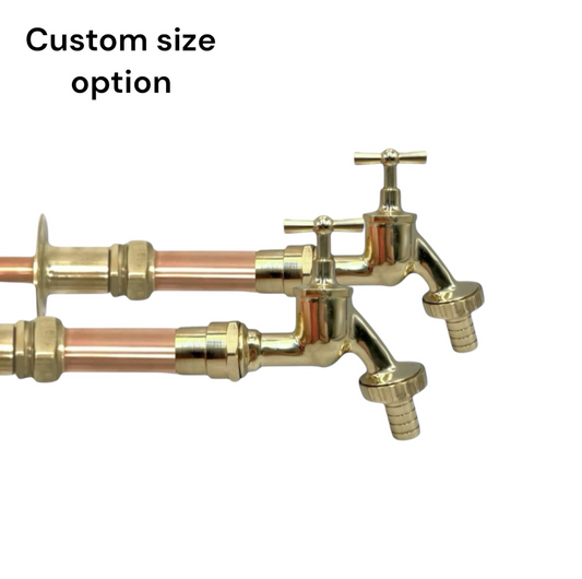 Pair of brass wall taps with copper pipework and detachable nozzles on a white background 