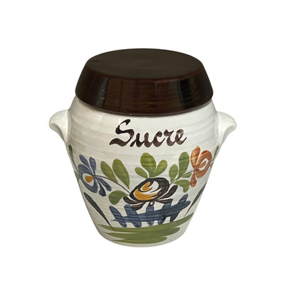 A small white ceramic jar with a dark brown lid, decorated with a hand-painted floral pattern and the word 'Sucre' in brown script on the front, set against a plain white background.