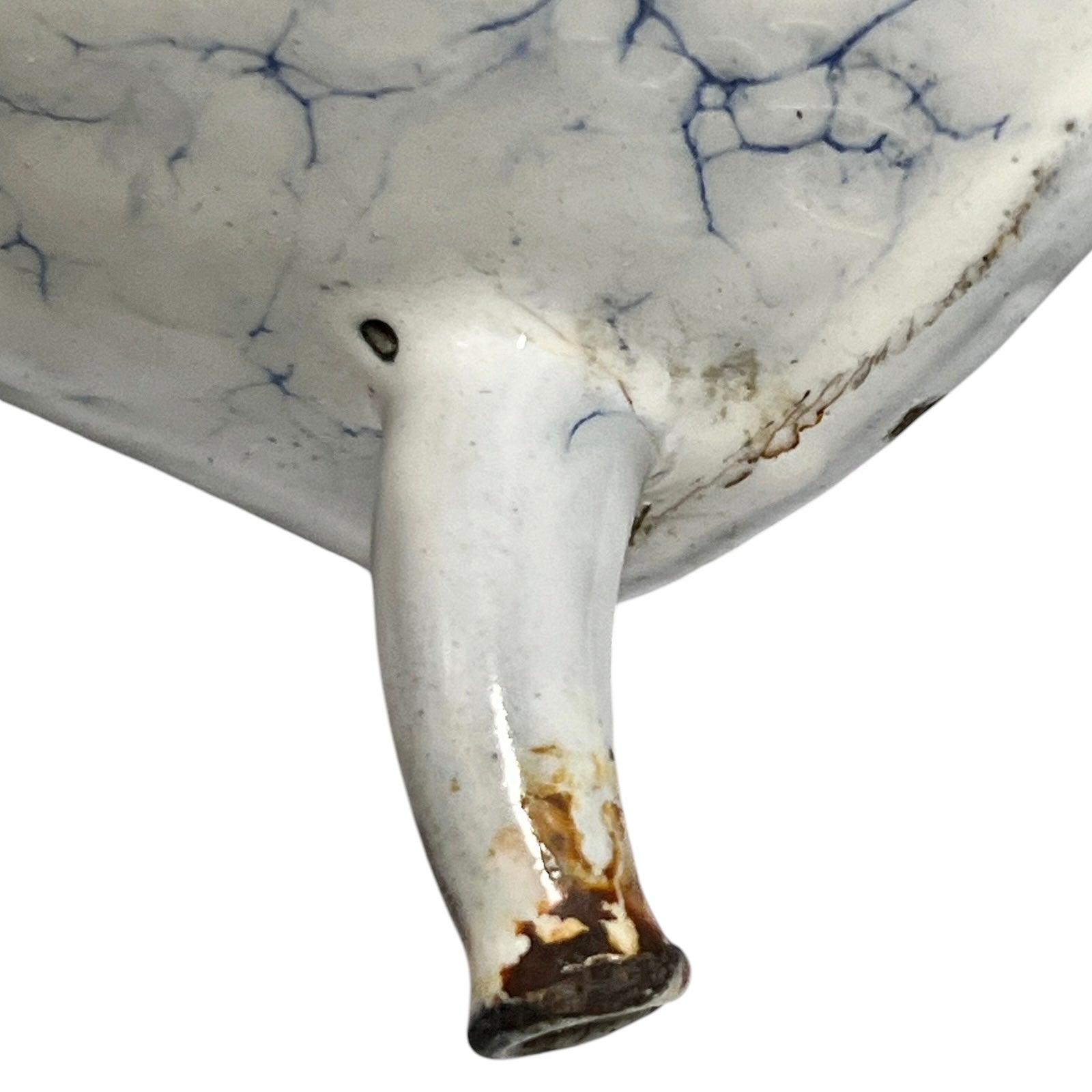 Close-up of a white ceramic vessel showing a glossy glazed surface with blue crackle-style veining and a small protruding spout photographed against a white background.