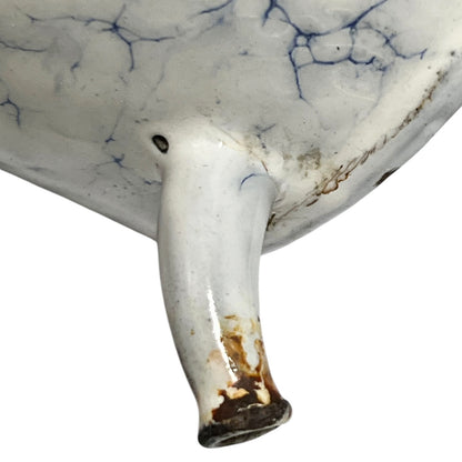 Close-up of a white ceramic vessel showing a glossy glazed surface with blue crackle-style veining and a small protruding spout photographed against a white background.