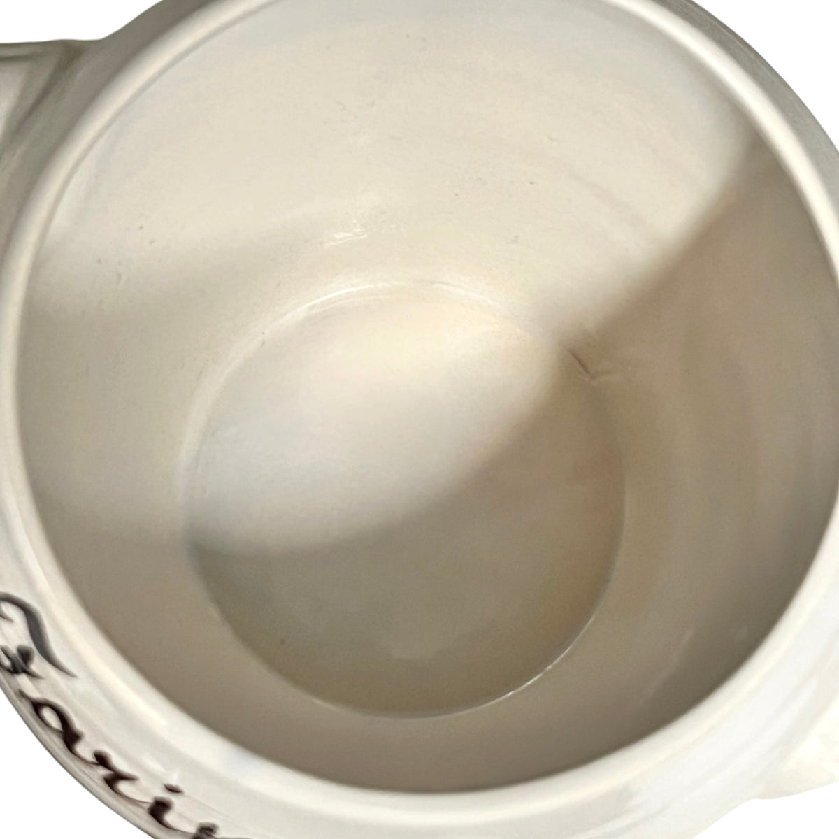 Close-up view inside a white ceramic mug or cup, showing the glossy interior surface and a small portion of dark script text near the lower left edge.