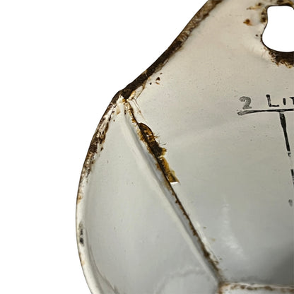 Close-up of a white enamel kitchen pot with a prominent cracked seam, rusted brown corrosion along the edges, and a measurement marking indicating 2 Liters.