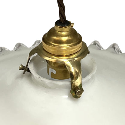 Close-up of a vintage white glass pendant light shade with a brass socket and hanging cord, shown against a white background.