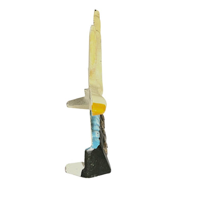A small decorative figurine or sculpture shaped like a stylized human figure, with a cream-colored upper body, a bright yellow accent, a blue section, and a dark base, isolated on a white background.