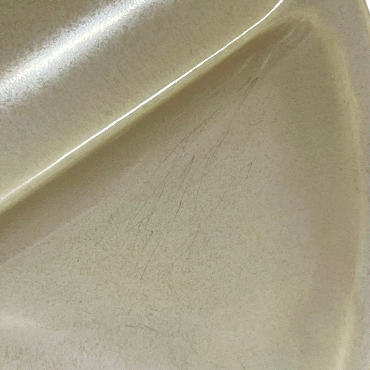 Close-up of a glossy cream-colored ceramic plate showing fine scratches on the surface.