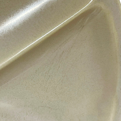 Close-up of a glossy cream-colored ceramic plate showing fine scratches on the surface.