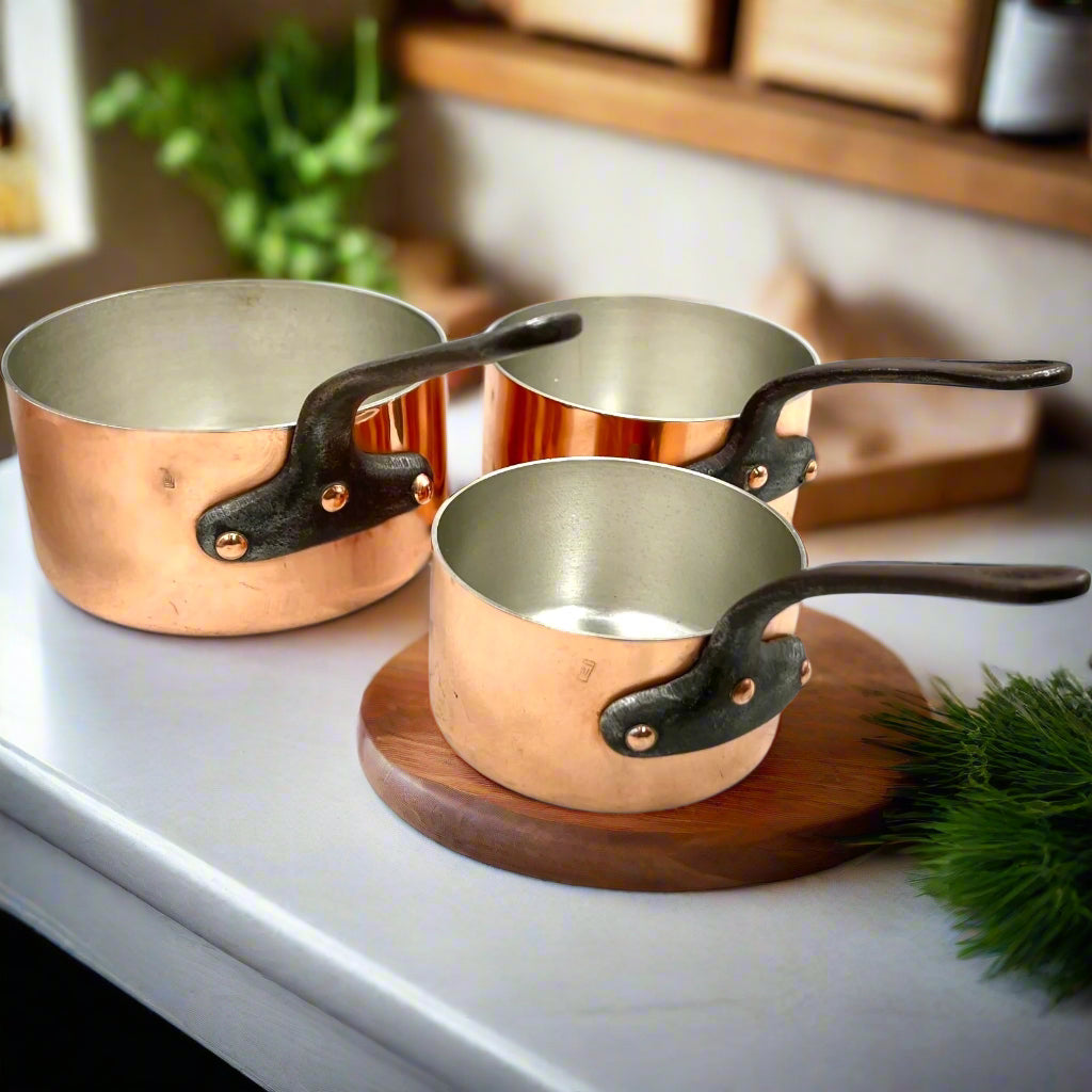 Set of three copper 2mm saucepans with new tin lining and black handles on table in a rustic kitchen