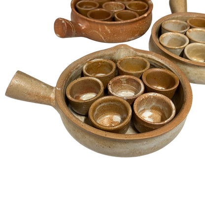 Three rustic handmade ceramic escargot sets with brown and beige glazes, featuring a small handle and multiple small cups inside, shown on a white background.