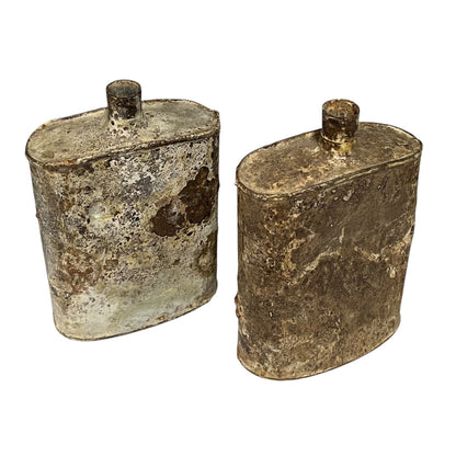 Pair of relic British WW1 metal water bottles in a rusty and flaky condition on a white background