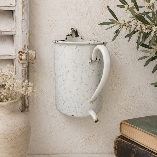 Vintage-style white enamel planter mounted on a textured wall with a rustic setting.