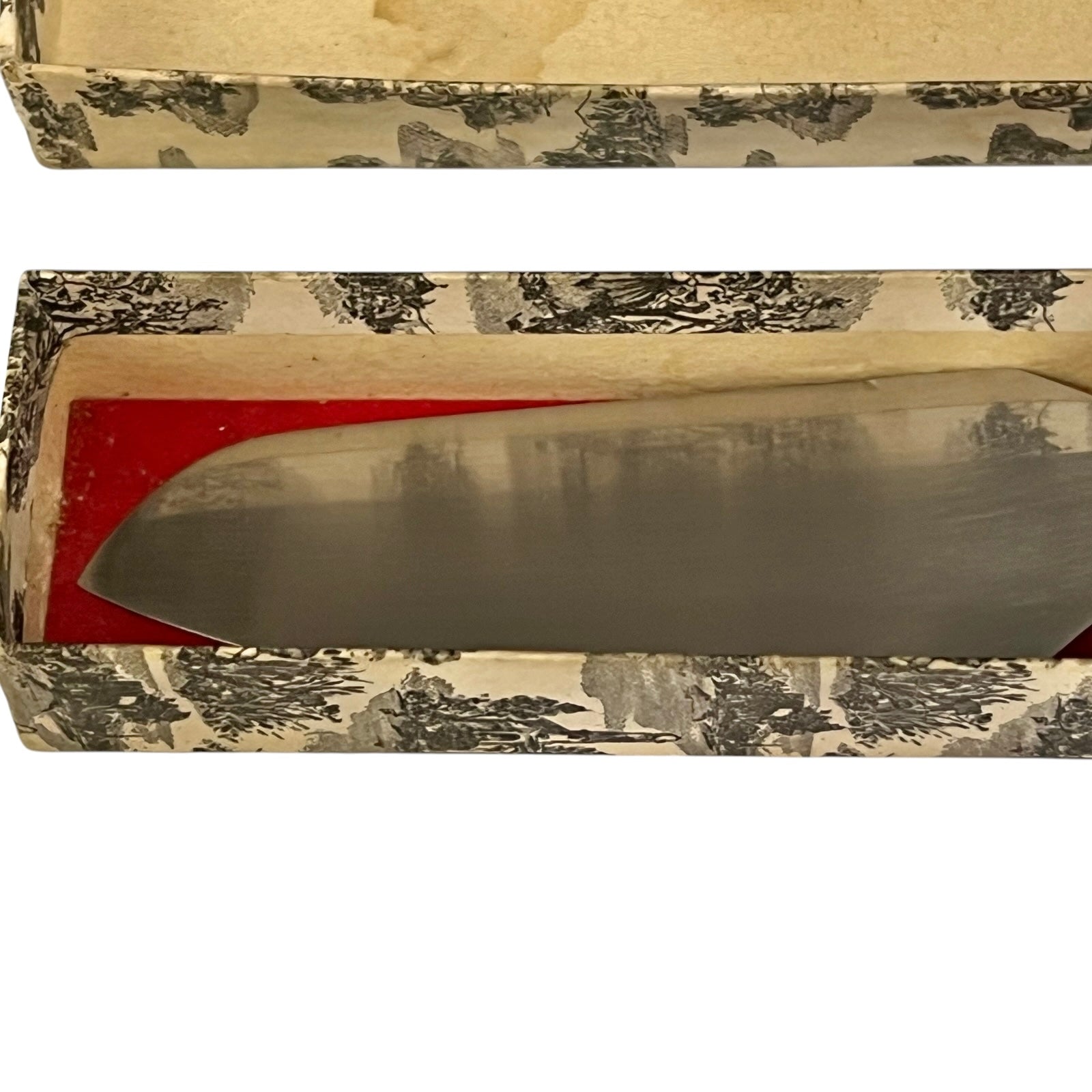 A large cake slice with a brushed silver blade resting inside an open vintage patterned box with a red interior lining.