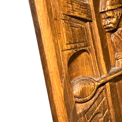 Wooden plaque with a carved design of a person holding a spoon.