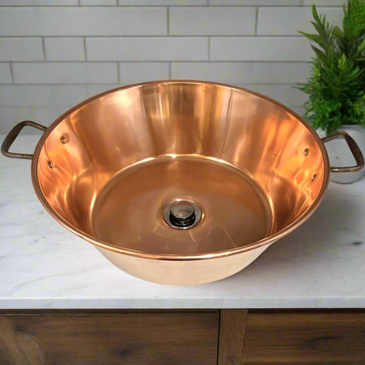 French copper bowl upcycled into a copper sink with iron handles and a chrome pop up waste on a vanity unit in a bathroom with a plant in the background