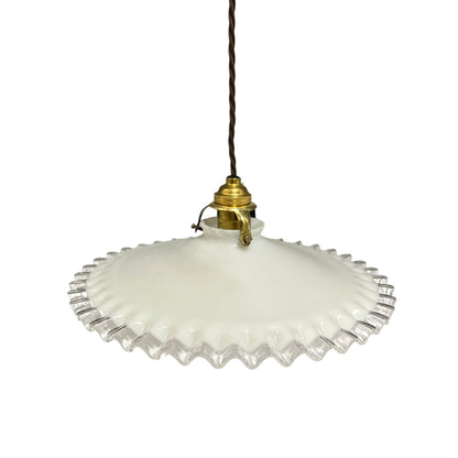 A vintage-style pendant light with a white ribbed glass shade featuring a scalloped, fluted edge, suspended from a brass fixture on a dark brown cord, shown against a plain white background.