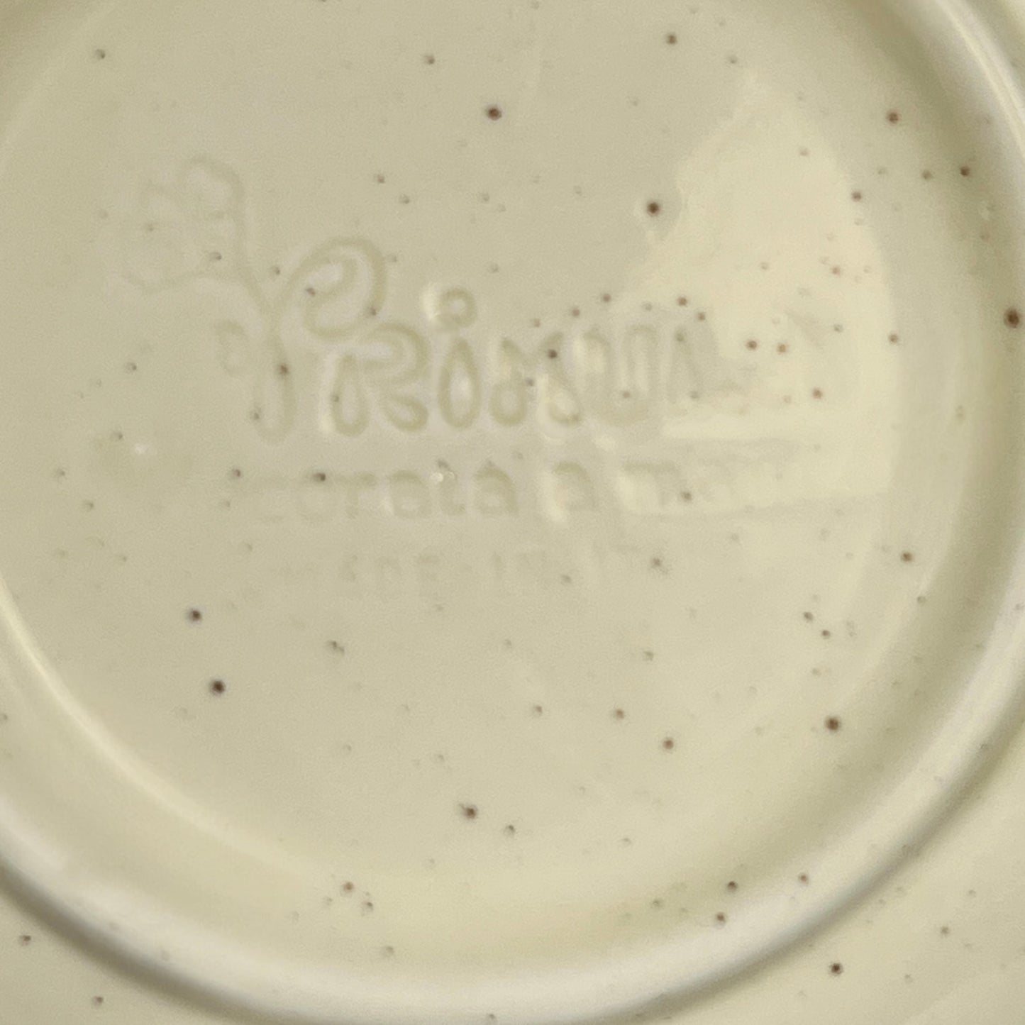 Close-up of a ceramic plate with speckled pattern and 'Primula' branding.