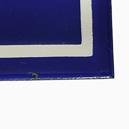Close-up of a blue square tile or sign corner with a white painted border on a white background.