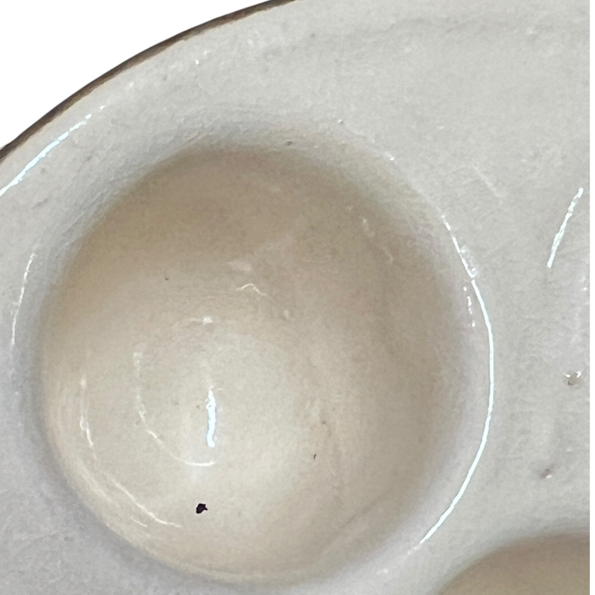 Close-up of a glossy ceramic escargot dish showing a shallow cream-colored well with a smooth glazed finish.