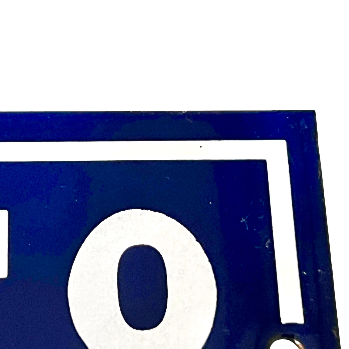 Close-up of a dark blue sign or plaque with a large white circular letterform and a white border line, cropped tightly against a white background.