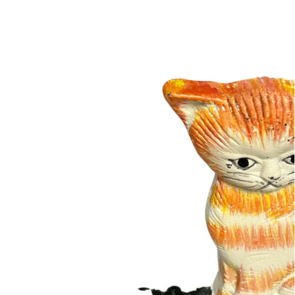 A close-up of a hand-painted cast iron cat figurine with orange and cream stripes, shown on a plain white background.