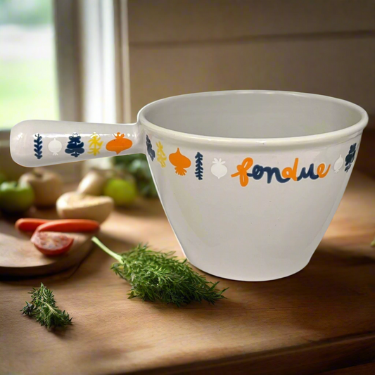 Vintage Le Creuset cast iron pan with 'fondue' text and tree designs on a wooden surface with herbs and vegetables for sale from All Things French Store.