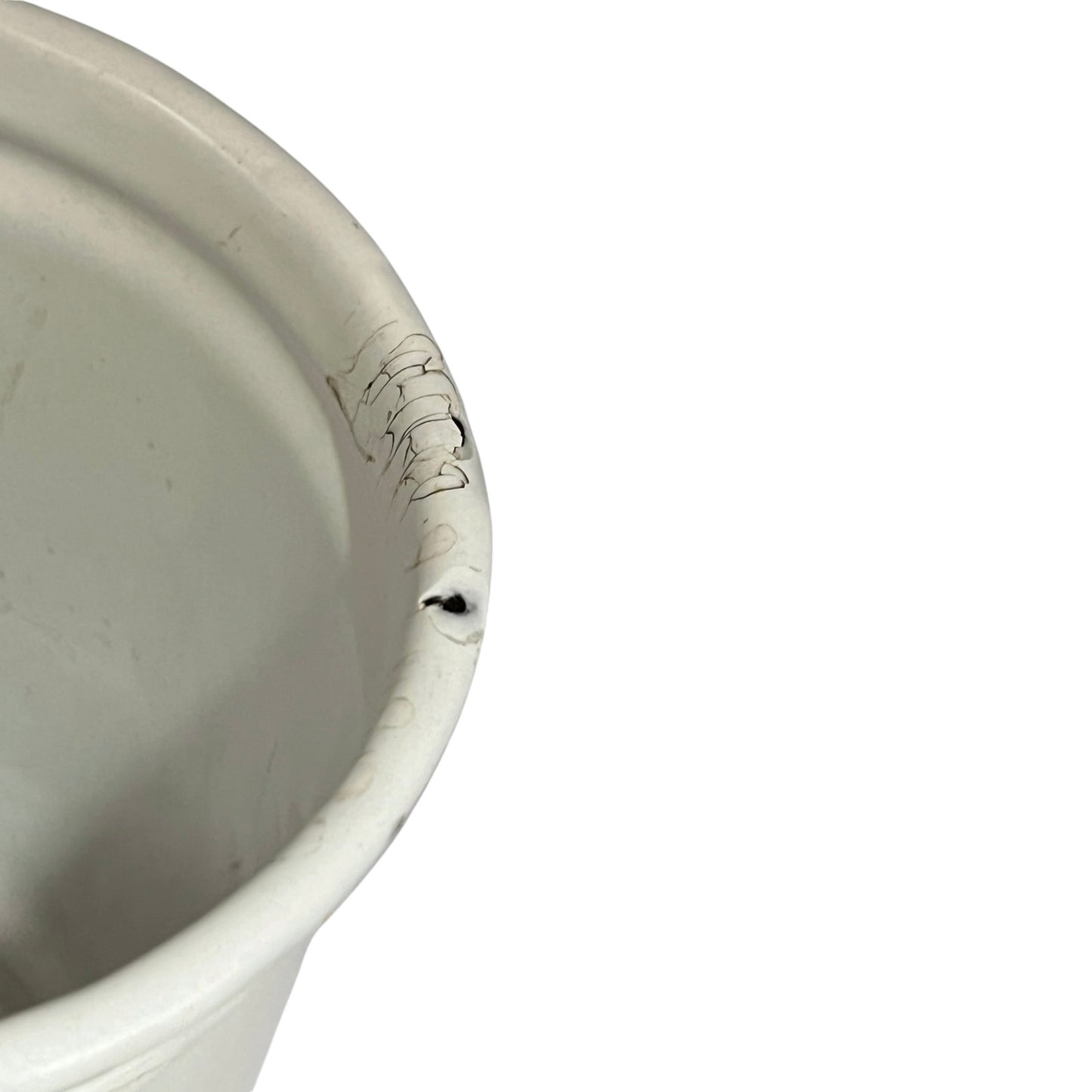 Close-up of a white enamel pot corner showing a small dark chip or scuff on the rim against a white background.