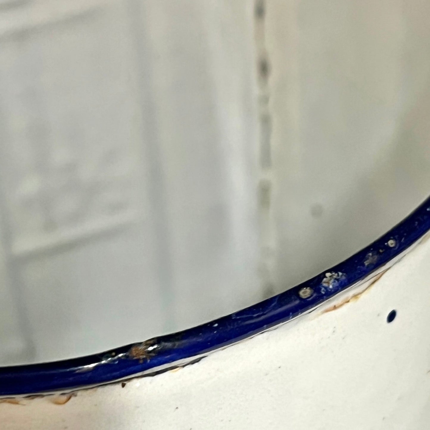 Close-up of a white enamel surface with a glossy dark blue rim, showing some wear, scuffs, and dirt along the edge.