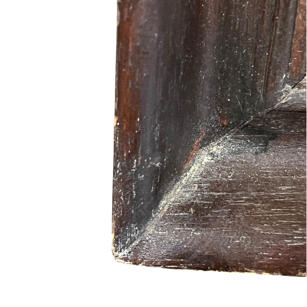 Close-up detail of a dark brown wooden furniture corner showing the grain, wear, and scuffs on a white background.