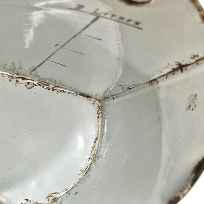 Close-up of the interior bottom of a white enamel measuring vessel or bowl, showing a visible crack, chipped glaze, and printed measurement markings including '2 LITRES'.