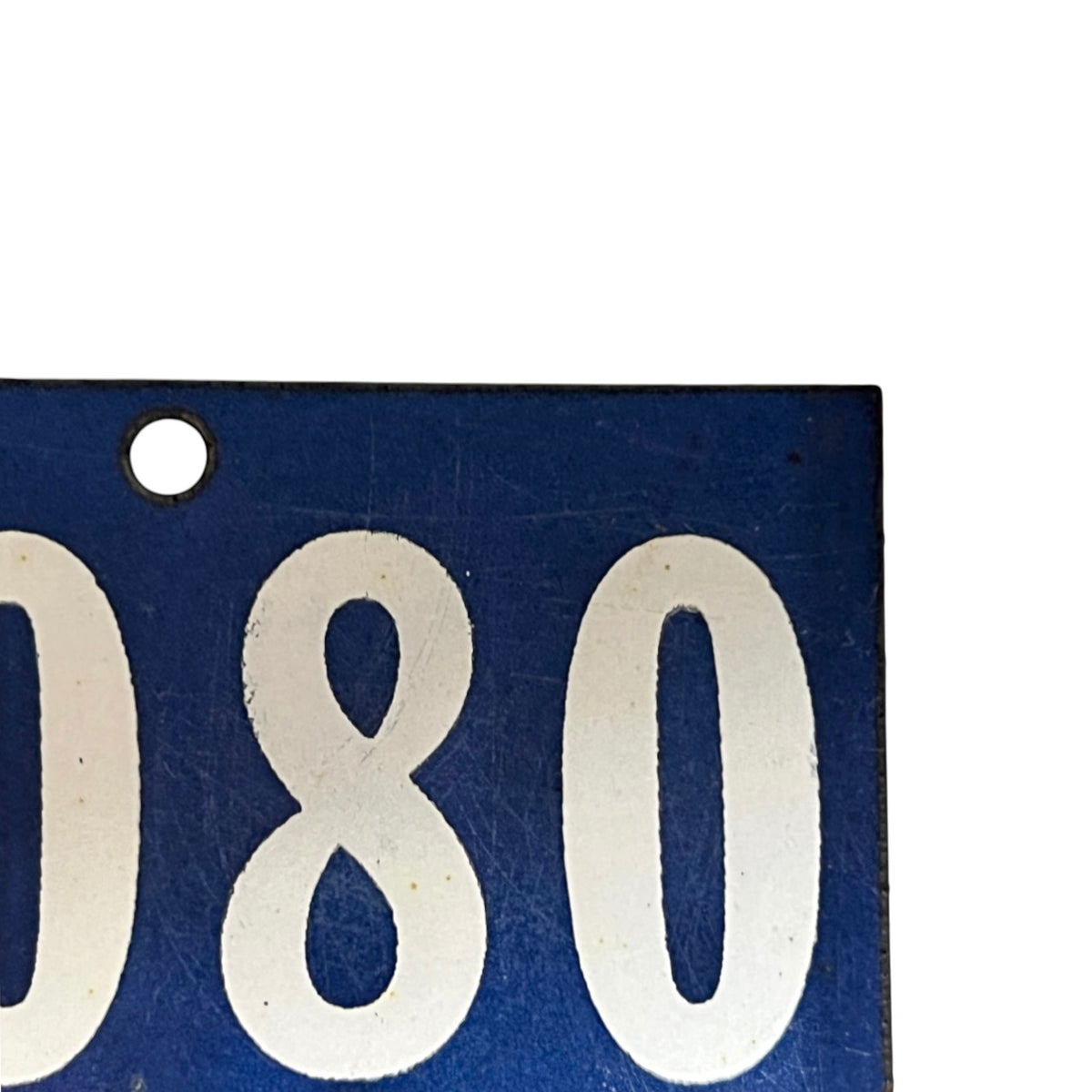 Close-up of a blue rectangular plate or tag with large white numerals '080' and a round mounting hole at the upper left, shown against a white background.