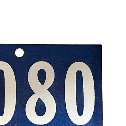 Close-up of a blue rectangular plate or tag with large white numerals '080' and a round mounting hole at the upper left, shown against a white background.