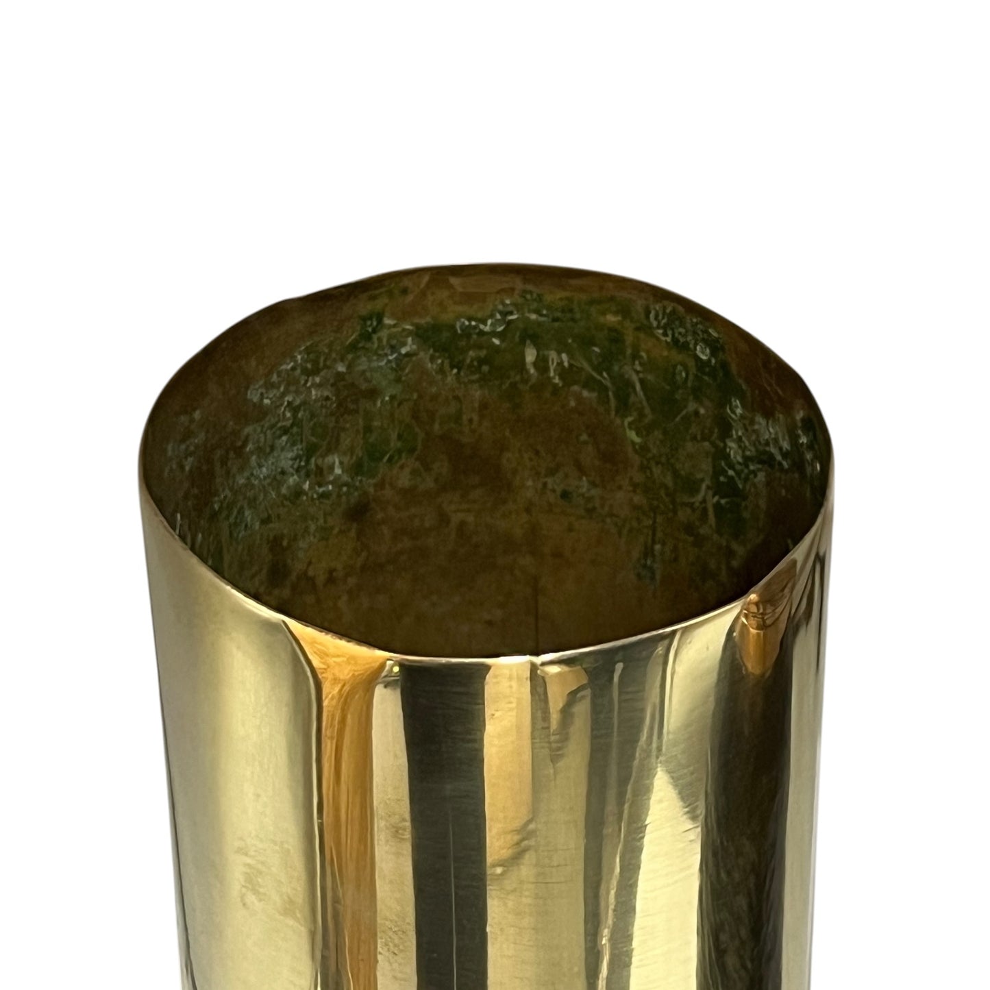 A close-up of a polished brass cylindrical container or vase, showing a reflective metallic gold exterior and a dark green patina inside, set against a plain white background.