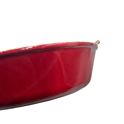 A close-up of a glossy red  baking dish or casserole dish on a plain white background.