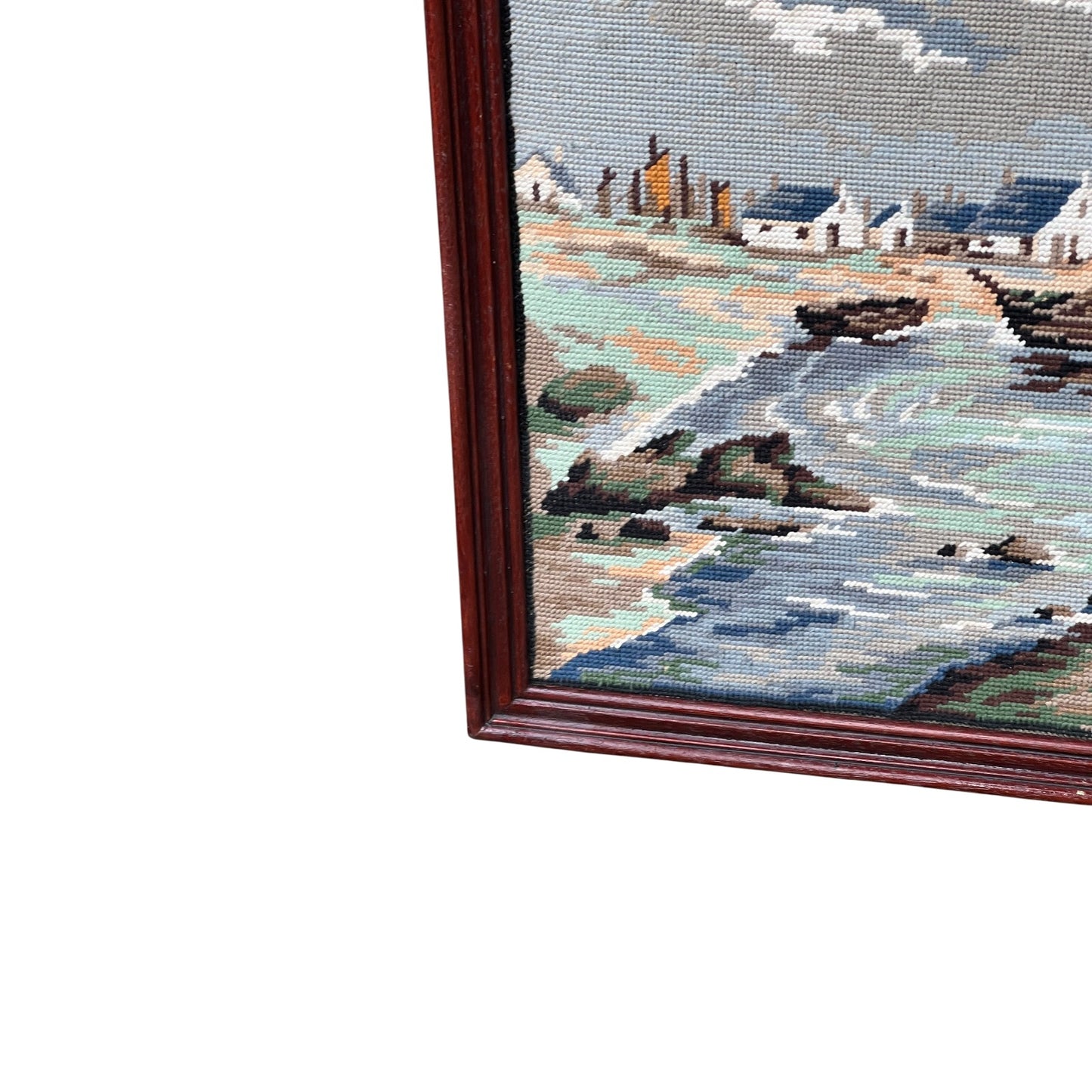 Close up of framed tapestry needlepoint with a coastal scene and wooden frame on a white background